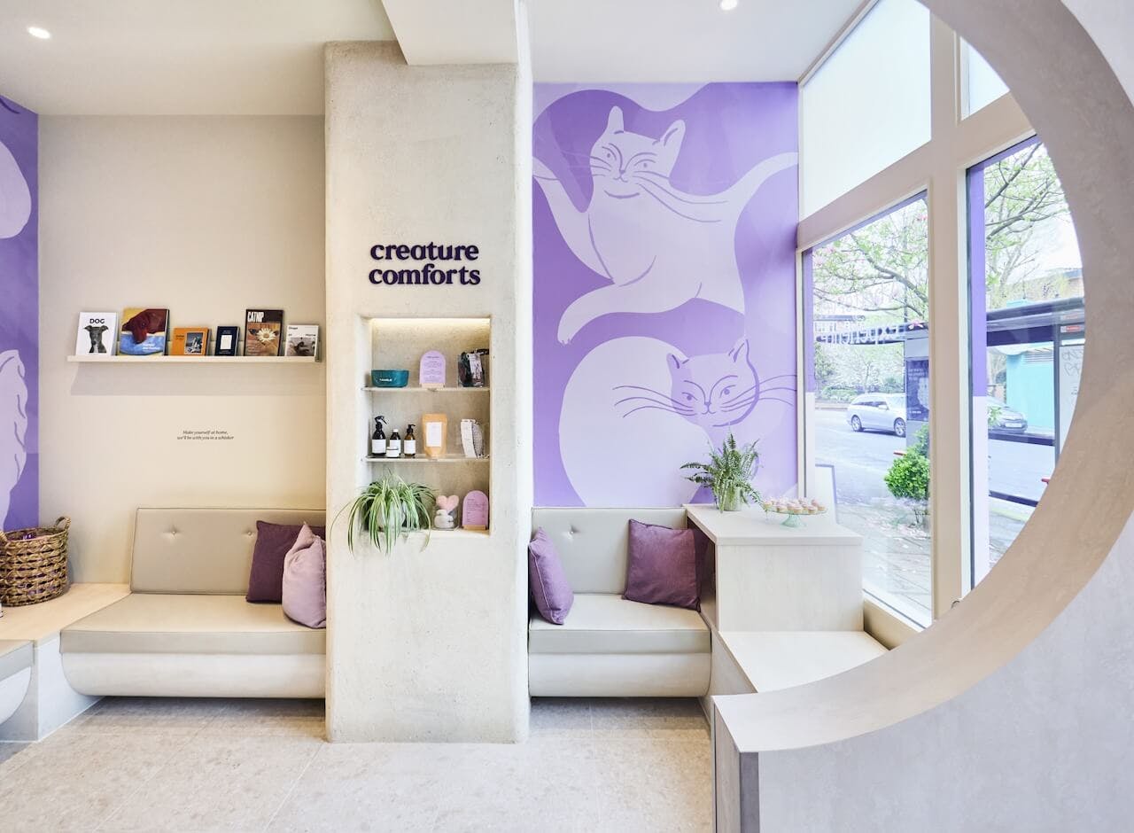 A bright interior view of Creature Comfort's Notting Hill clinic with welcoming sofas, pet toys and Creature Comforts branding on the wall. 